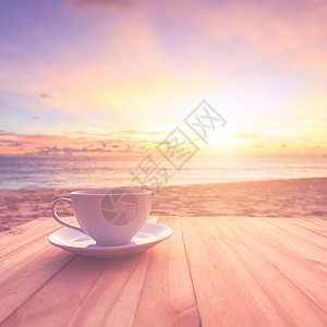 在日落或日出海滩的木桌上用透镜照明弹关闭咖啡杯热到效果Retr图片