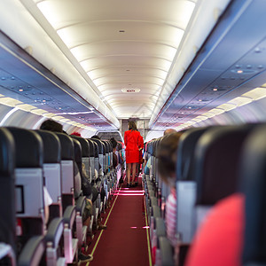 飞机内有乘客坐在座位上和穿红色制服的空姐图片
