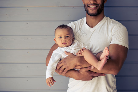 英俊的年轻非裔美国父亲在抱着他可爱的小宝时微图片