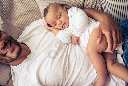 英俊的年轻非裔美国父亲在婴儿怀着双臂睡觉时笑着微图片
