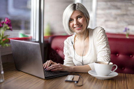 快乐的金发女人有笔记本电脑喝咖啡和做生意图片