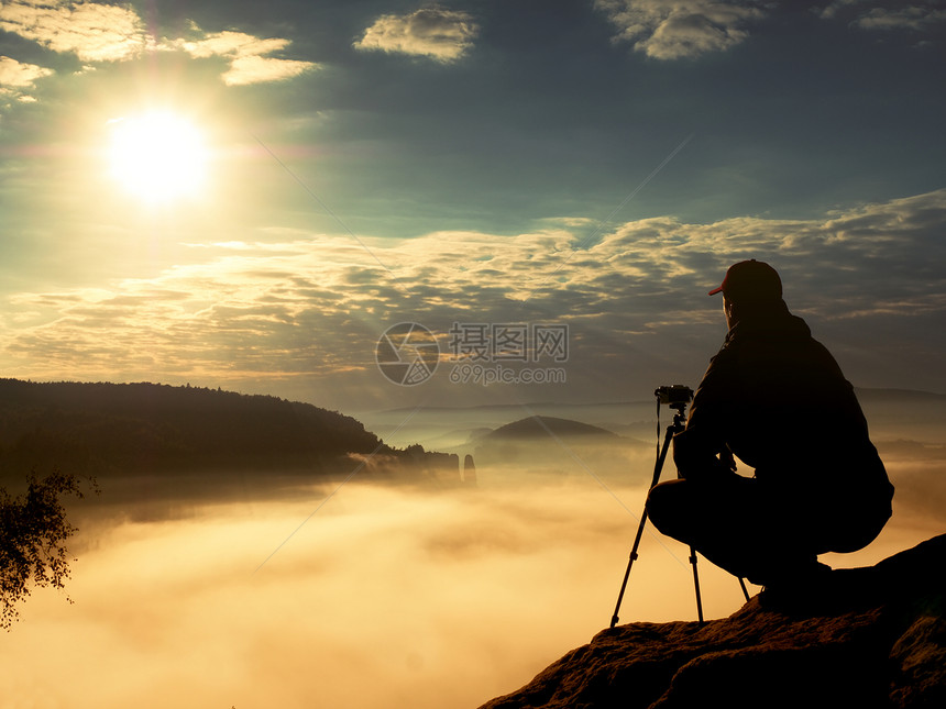 业余摄影师在岩石峰顶用相机拍照图片