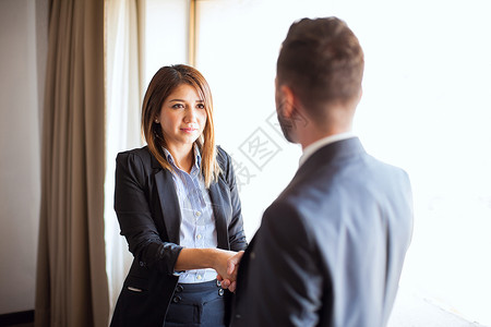 一位年轻商人在面试职位时与一位女招聘人员握手的观点图片