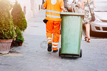 穿橙色制服的清洁公司工人和绿色垃圾桶图片