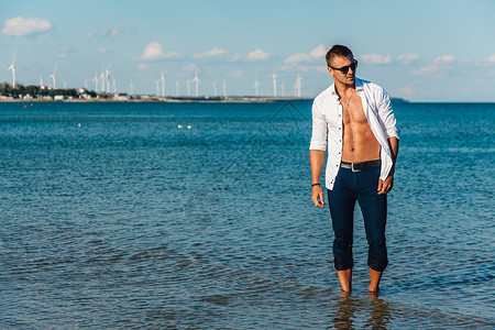 沙滩上散步的人一个穿着解开扣子的白衬衫在海滩上的年轻人脚在水里图片