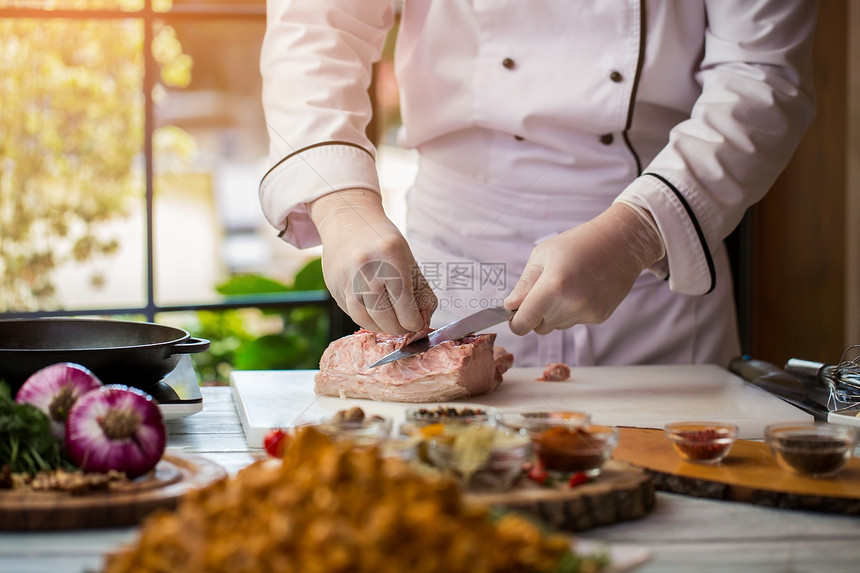 男人在切生肉穿白制服做饭厨师准备猪肉吃图片