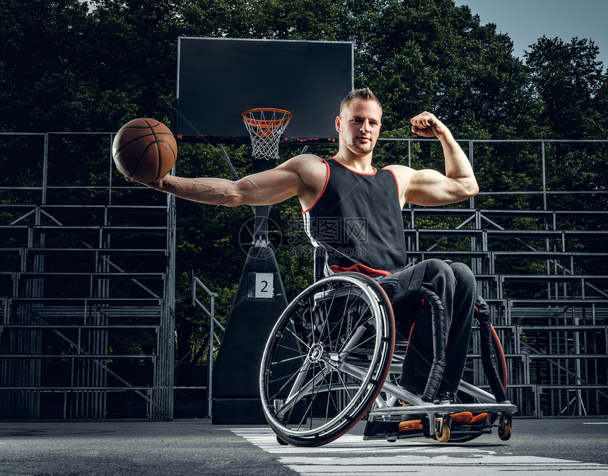 坐在轮椅上的残废篮球运动员在空地上拿着球图片