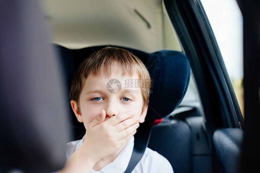 坐在儿童座椅上的汽车后座上的7岁小孩用手捂住嘴患有晕车图片
