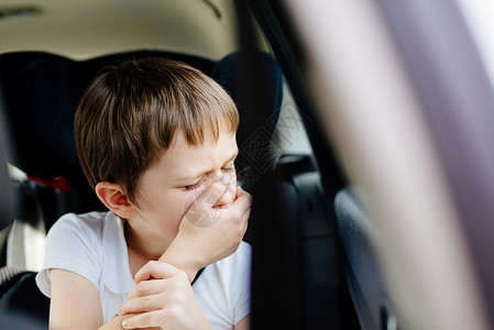 坐在儿童安全座椅上的汽车后座上的7岁小孩用手捂住嘴患有晕车背景