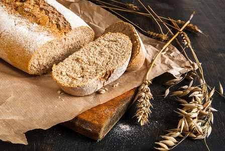黑色的木桌上有香味的新鲜出炉的黑麦面包面包被切片小麦和黑麦的小穗闭图片