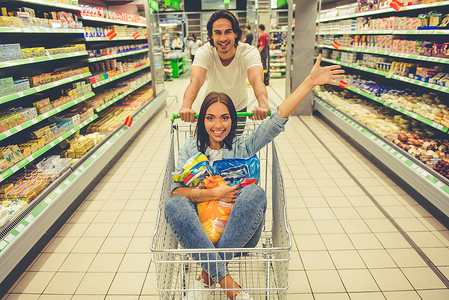 美丽的年轻夫妇在超市中选择食物时正在取乐图片