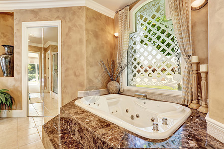 美丽的米色豪华大理石浴室内饰带台阶的大浴缸和装饰精美的大窗户图片