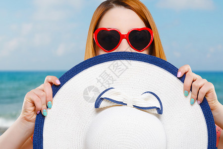 戴着心形红色太阳镜的女孩拿着帽子半张脸被帽子遮住夏天的样子以大海图片