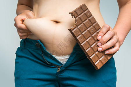 超重的女人穿牛仔裤拿着巧克力肥胖概念图片