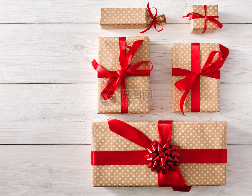 白色木背景上的礼品盒的顶部视图用红丝带蝴蝶结装饰的牛皮纸礼物圣诞节和其他假期的概念图片