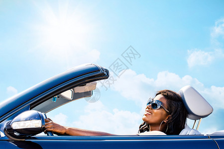 在阳光的天空下驾着敞篷轿车的迷人优雅的非洲女人图片