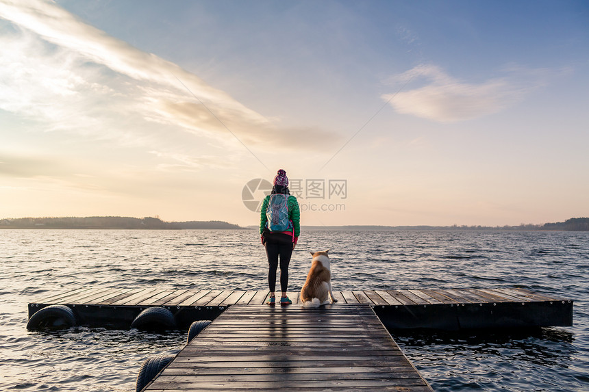 带着狗的女人享受日出和湖泊图片
