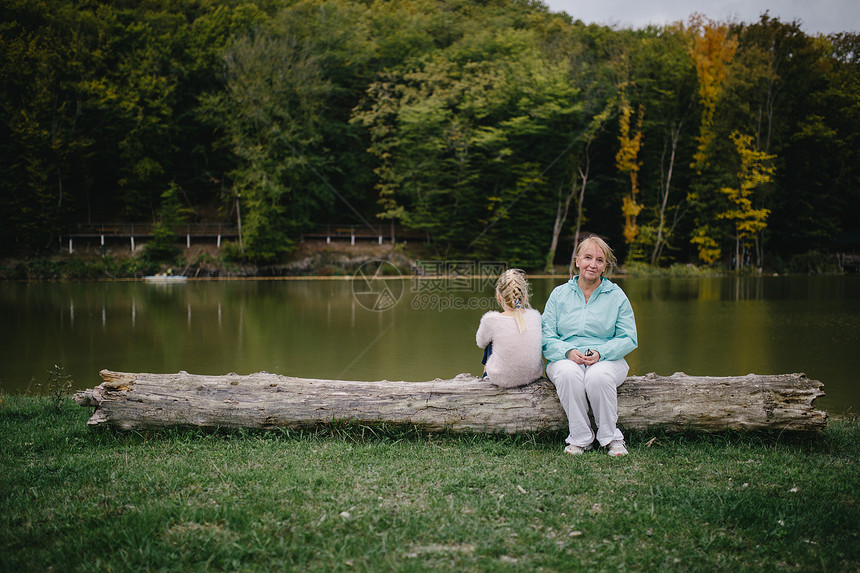 小女孩背弃了老妇人被冒犯的女孩和一位老妇坐在湖边的一根圆木上世代的冲图片