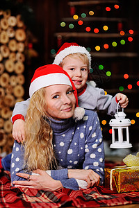 母亲和儿子戴着红色圣诞老人帽躺在圣诞灯上的方格毯子上拿着手电筒的一顶图片