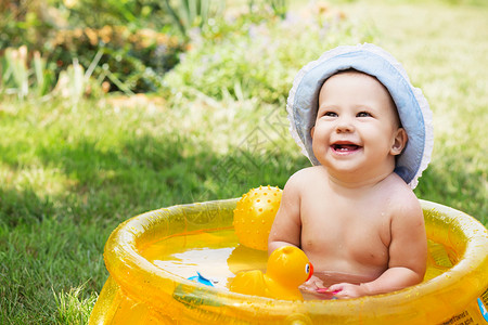 棉花巴拿马Cap浴池中美丽的女婴在炎热的夏日露户外的黄色充气图片
