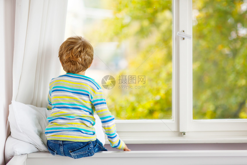 金发小男孩坐在窗边看雨滴图片