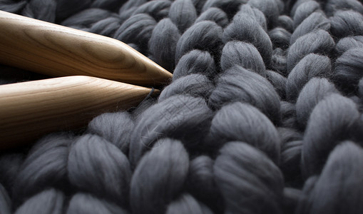 灰色美利奴羊毛毯背景上的木织针图片