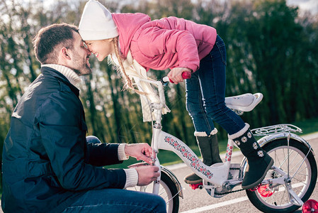 父亲在公园里玩乐时检查他女儿的自行车图片