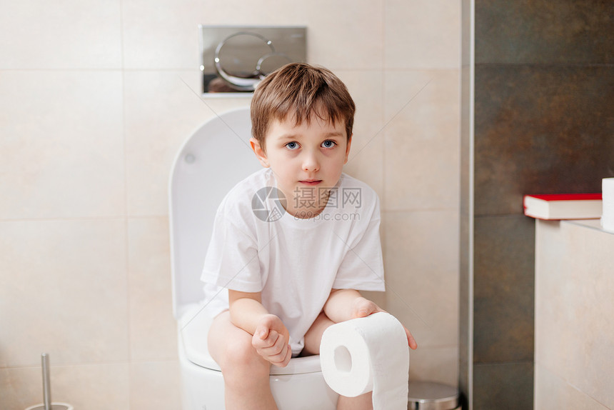 7岁小男孩坐在马桶上拿着白色卫生纸图片