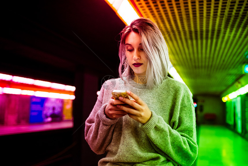 年轻美丽的白种人紫灰色头发女人在城市户外地铁上使用智能手机持图片