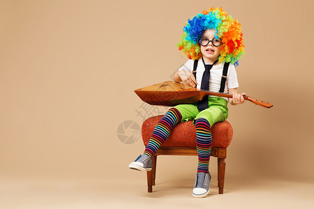 快乐的孩子们戴着大霓虹色假发弹巴拉莱卡和的快乐小丑男孩戴着小丑假发和眼镜背景图片