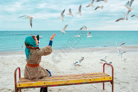 秋天多云的海边喂海鸥的女人图片