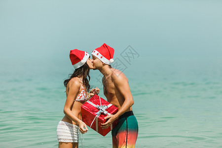 庆祝圣诞节和新年的轻美夫妇拿着红礼盒站在水里在图片