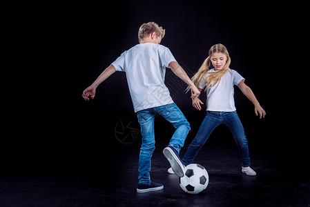 快乐的哥和妹玩足球在黑色孤背景图片
