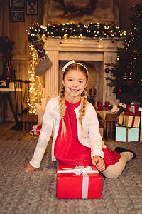 微笑的女孩坐在地毯上有圣诞礼物在场图片