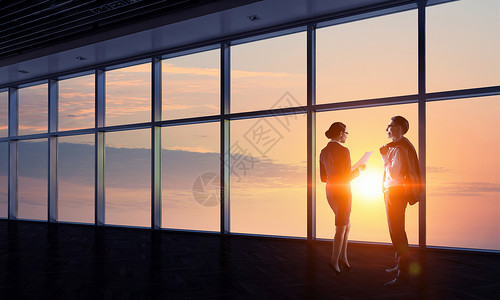 在日出与全景窗口对面的日出中两个商业人图片