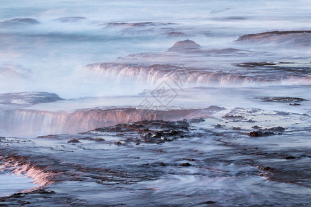 以缓慢的百叶窗速度捕捉到的粗海创造了一个舒缓的场景水流过熔岩石并产生平背景图片