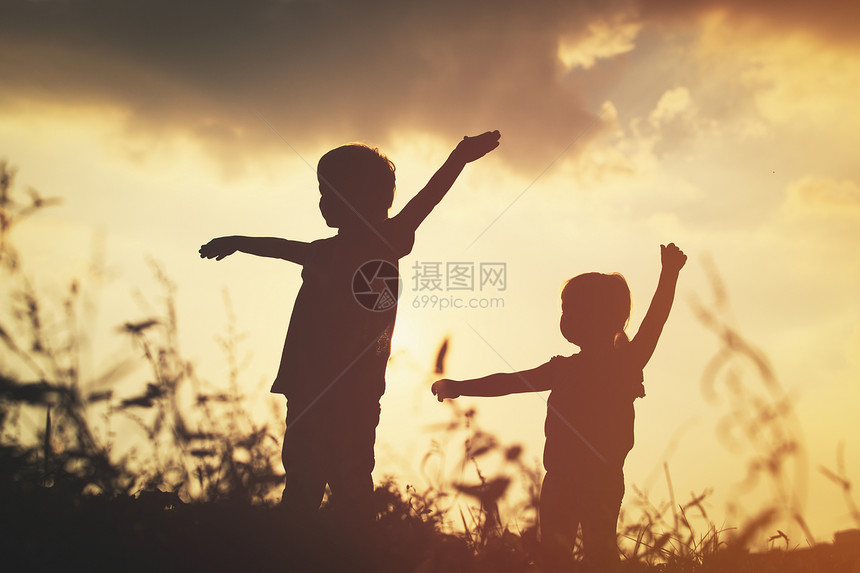 小男孩和女孩的剪影在大自然的日落时分玩耍图片