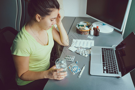 女人坐在笔记本电脑前看药片图片