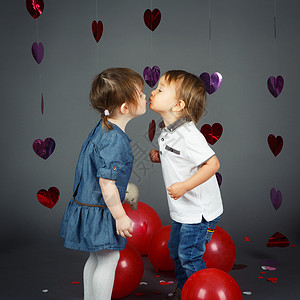 两个可爱的孩子在工作室里用灰色背景的红心和气球亲吻的肖像图片