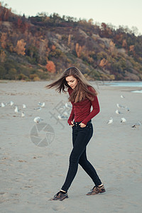 快乐的笑着兴奋的白人年轻女子穿着牛仔裤奔跑在秋日的海鸥鸟中跳跃图片