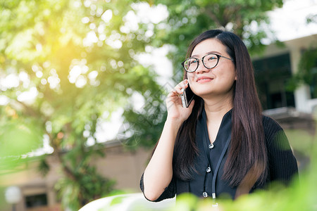 快乐的亚洲眼镜女人常在户外用智能电话聊天图片