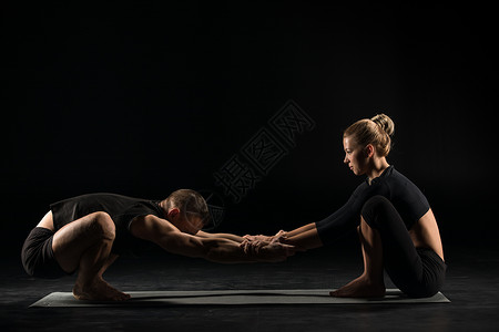 年轻夫妇在瑜伽垫上做伸展锻炼在孤立于黑边图片