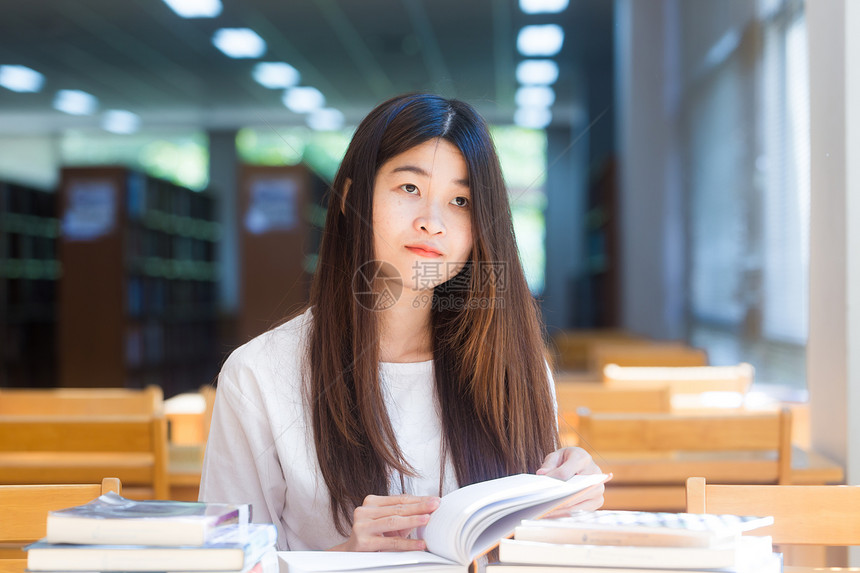 快乐女学生在图书馆阅读书时坐在窗外的木椅子上图片