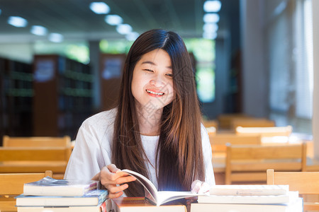 一个年轻有魅力的亚洲女人在图书馆坐着看书的画图片