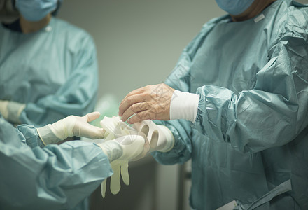 医院手术的外科医生在手术室急诊室的手术室中戴上无菌制服图片