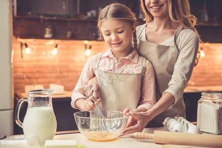 可爱的小女孩和她美丽的妈穿着围裙在家厨房做烘烤时在图片
