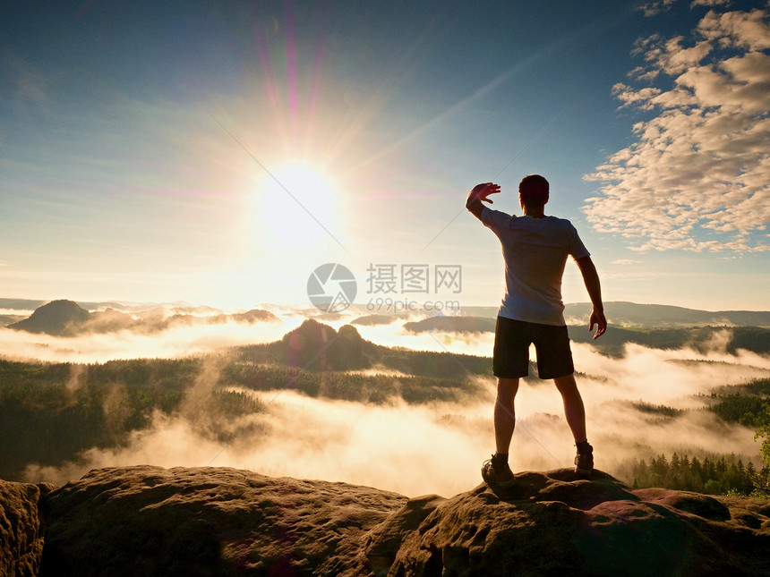 年轻的运动员从日出太阳的明亮光照耀着他的眼睛山顶成就岩石中的图片