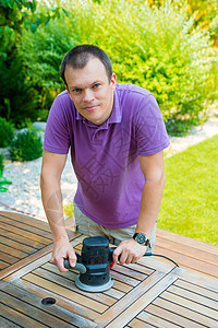年轻人木匠在花园里用电动砂光机工作用图片