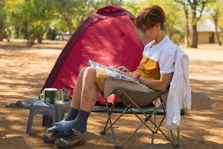 女人在露营地放松时阅读杂志帐篷椅子和野营装备夏季户外活动在南非图片