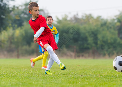 男孩在运动场上踢足球背景图片